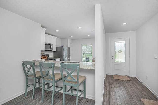 kitchen with white cabinetry, a healthy amount of sunlight, dark wood-type flooring, stainless steel appliances, and a kitchen bar