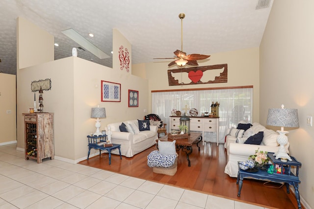 living room with ceiling fan, light tile patterned floors, a textured ceiling, and high vaulted ceiling