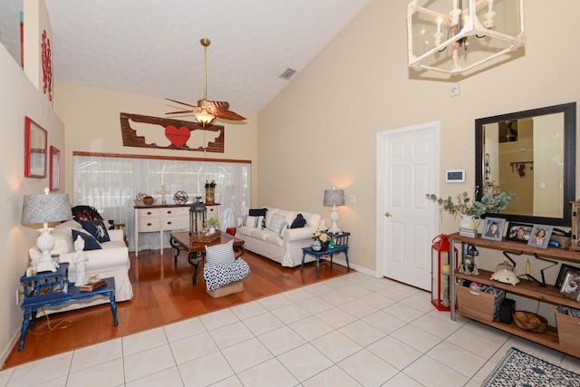 tiled living room featuring ceiling fan with notable chandelier and high vaulted ceiling