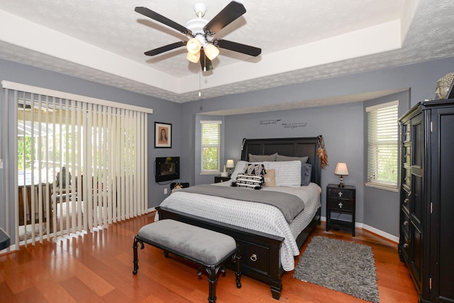 bedroom featuring hardwood / wood-style floors, a tray ceiling, ceiling fan, and access to outside