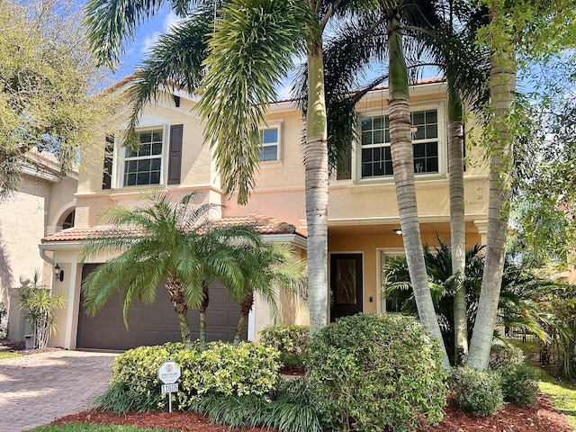 view of front of property featuring a tiled roof, decorative driveway, an attached garage, and stucco siding