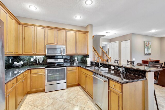 kitchen with kitchen peninsula, stainless steel appliances, decorative backsplash, light brown cabinets, and a breakfast bar