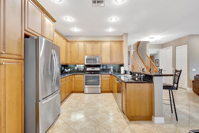 kitchen with kitchen peninsula, a breakfast bar area, stainless steel appliances, dark stone counters, and sink