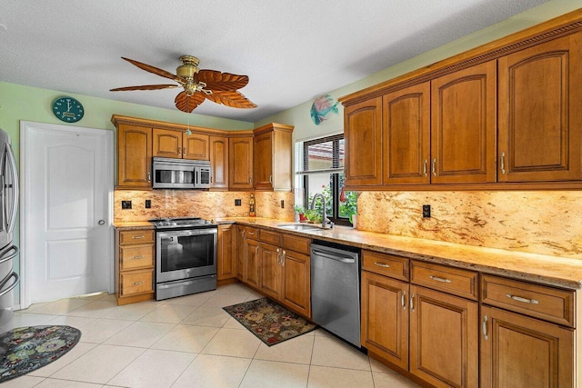 kitchen featuring light tile patterned floors, stainless steel appliances, tasteful backsplash, light stone counters, and sink