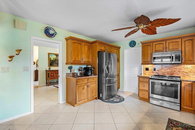 kitchen with a textured ceiling, light tile patterned floors, appliances with stainless steel finishes, and decorative backsplash