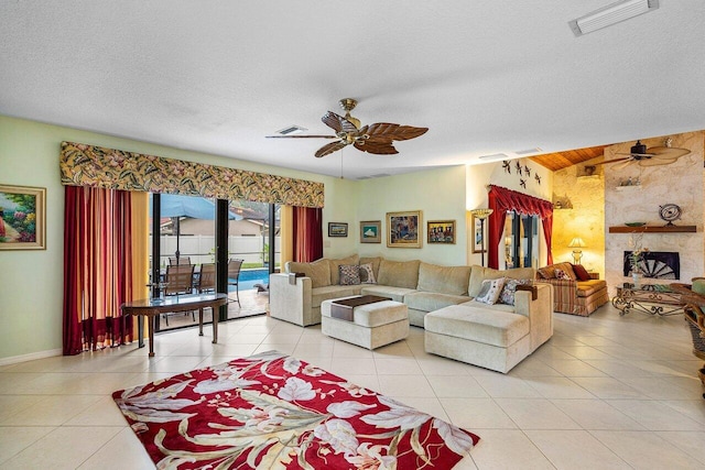 tiled living room featuring a textured ceiling, ceiling fan, and a stone fireplace