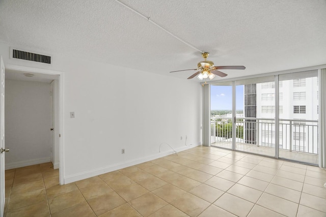 tiled empty room with ceiling fan, expansive windows, and a textured ceiling