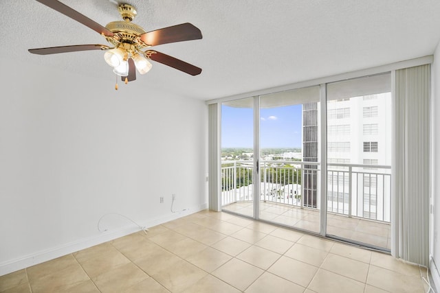 empty room featuring plenty of natural light, ceiling fan, light tile patterned floors, and floor to ceiling windows