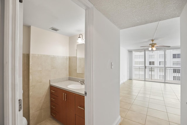 bathroom with vanity, tile patterned floors, a textured ceiling, tile walls, and a wall of windows