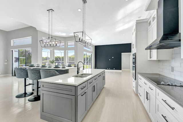 kitchen featuring wall chimney exhaust hood, white cabinetry, sink, backsplash, and hanging light fixtures