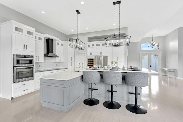 kitchen featuring decorative light fixtures, wall chimney range hood, white cabinetry, a large island, and french doors