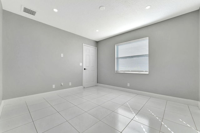 empty room with a textured ceiling and light tile patterned floors