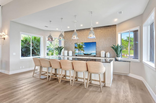 kitchen with a kitchen bar, hanging light fixtures, white cabinets, and light hardwood / wood-style flooring