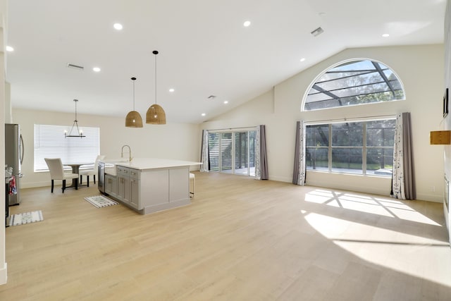 kitchen with gray cabinets, light hardwood / wood-style flooring, hanging light fixtures, an island with sink, and stainless steel appliances