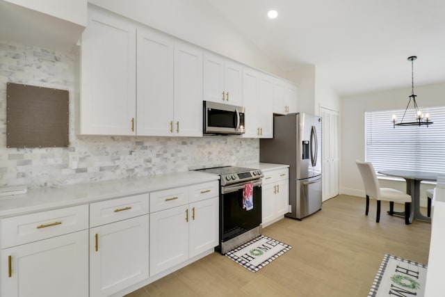 kitchen with vaulted ceiling, stainless steel appliances, white cabinets, and hanging light fixtures