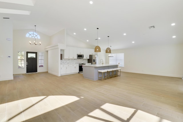 kitchen with tasteful backsplash, appliances with stainless steel finishes, a center island with sink, and hanging light fixtures