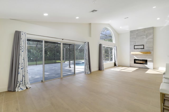 unfurnished living room featuring high vaulted ceiling, light hardwood / wood-style flooring, and a tiled fireplace