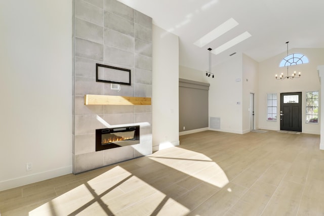 unfurnished living room featuring high vaulted ceiling, a tile fireplace, and a notable chandelier