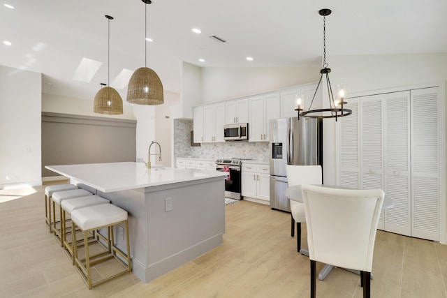 kitchen with decorative light fixtures, backsplash, appliances with stainless steel finishes, and a center island with sink