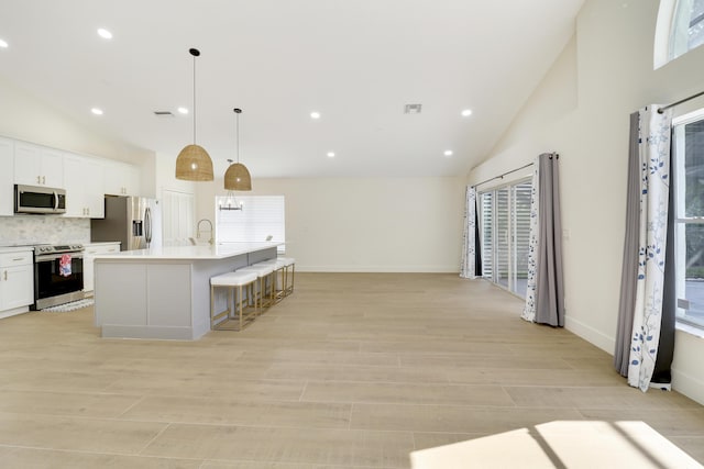 kitchen with white cabinetry, a center island with sink, appliances with stainless steel finishes, backsplash, and hanging light fixtures