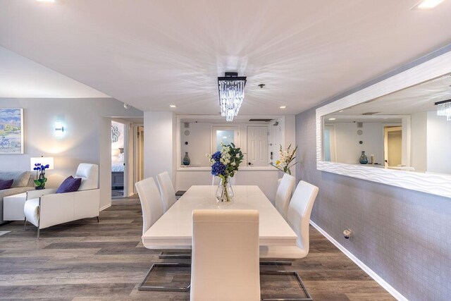 dining area featuring dark wood-type flooring, brick wall, and an inviting chandelier