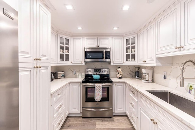 kitchen with white cabinets, appliances with stainless steel finishes, light stone counters, and sink