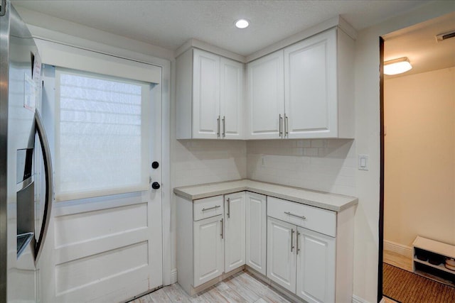 kitchen with stainless steel refrigerator with ice dispenser, light wood-type flooring, tasteful backsplash, a textured ceiling, and white cabinets