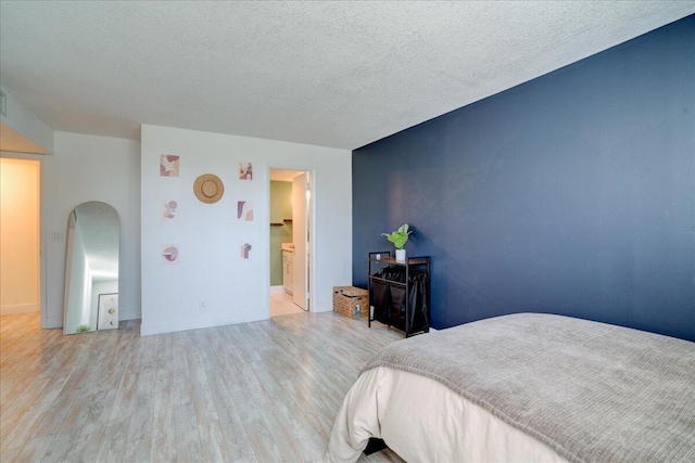 bedroom featuring a textured ceiling, light hardwood / wood-style floors, and ensuite bath