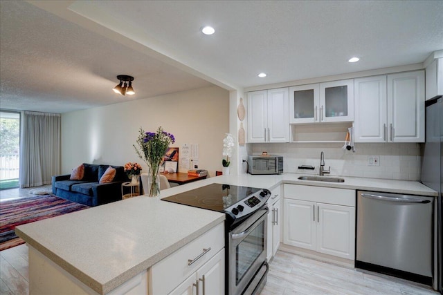 kitchen with kitchen peninsula, appliances with stainless steel finishes, backsplash, sink, and white cabinetry