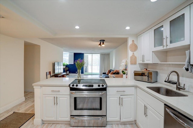 kitchen featuring kitchen peninsula, decorative backsplash, stainless steel appliances, sink, and white cabinets