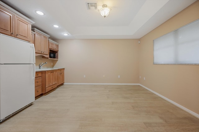 kitchen featuring a raised ceiling, sink, white fridge, and light wood-type flooring