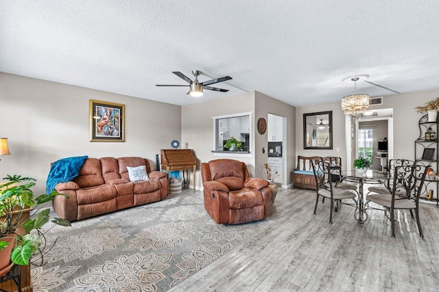 living room with ceiling fan with notable chandelier, light hardwood / wood-style floors, and a textured ceiling