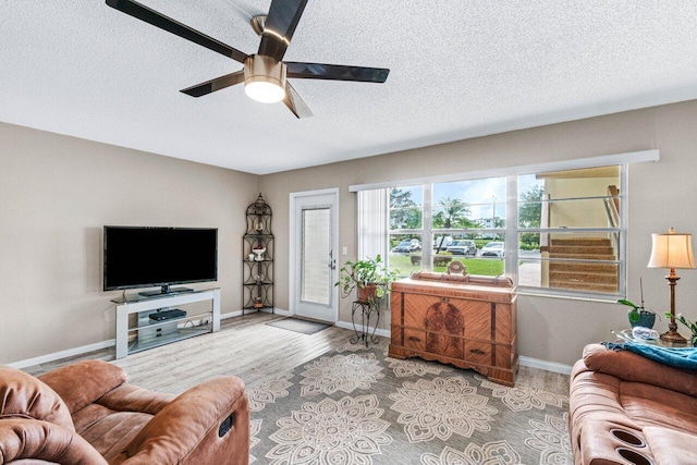 living room featuring ceiling fan, light hardwood / wood-style floors, and a textured ceiling