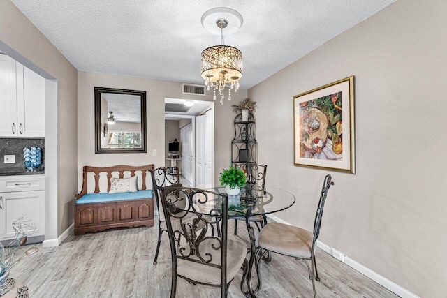 dining space with a chandelier, light wood-type flooring, and a textured ceiling