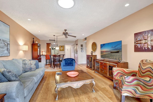 living room with ceiling fan, light hardwood / wood-style flooring, and a textured ceiling