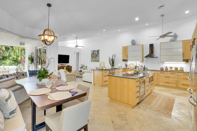 kitchen with wall chimney exhaust hood, light brown cabinets, ceiling fan with notable chandelier, and decorative light fixtures