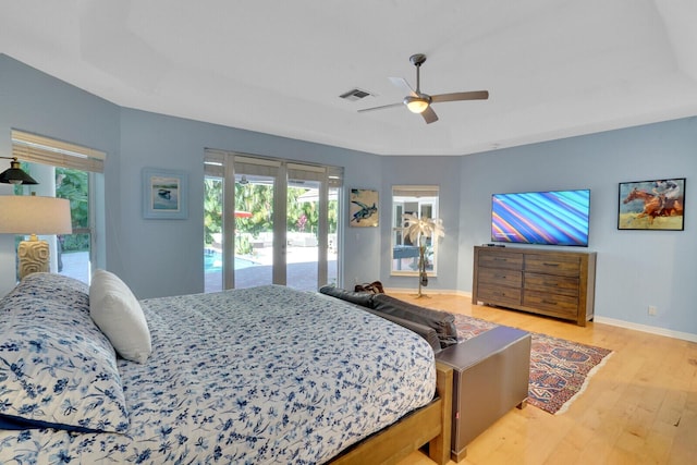 bedroom with access to exterior, light hardwood / wood-style floors, a raised ceiling, and ceiling fan