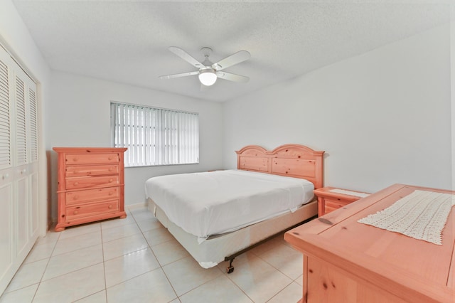 bedroom featuring ceiling fan, a textured ceiling, light tile patterned floors, and a closet