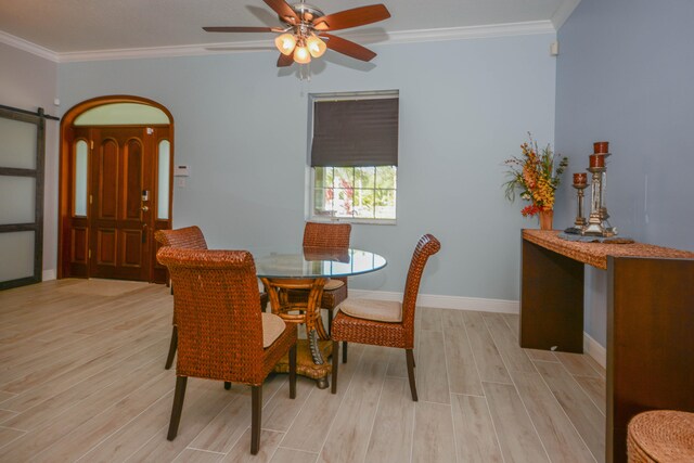 dining room featuring ceiling fan, light wood-type flooring, crown molding, and a barn door