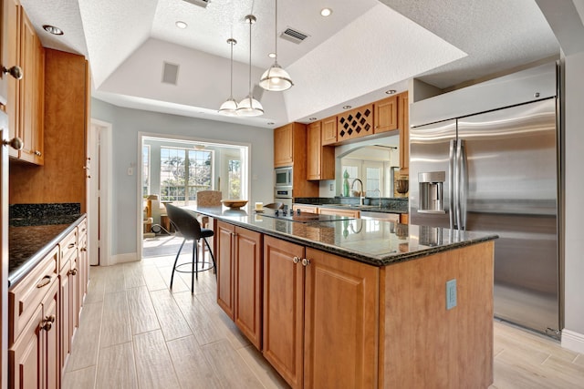 kitchen with built in appliances, a center island, a textured ceiling, dark stone counters, and hanging light fixtures