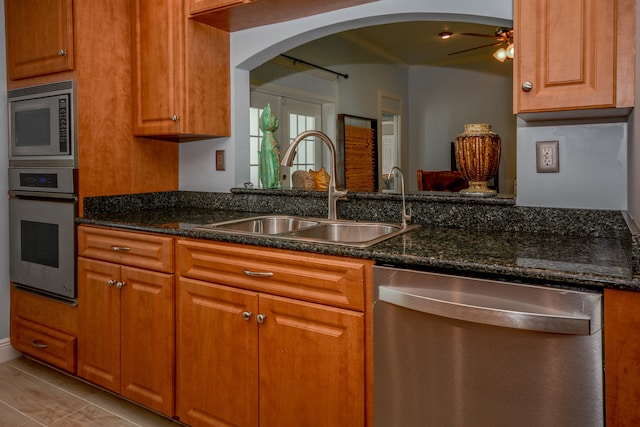 kitchen featuring ceiling fan, stainless steel appliances, sink, and dark stone countertops