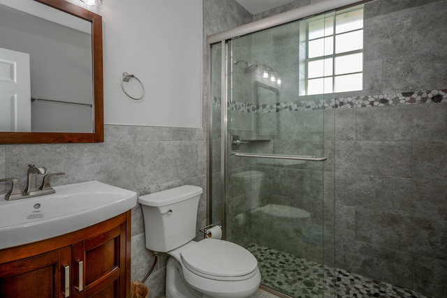 bathroom with vanity, toilet, a shower with shower door, and tile walls