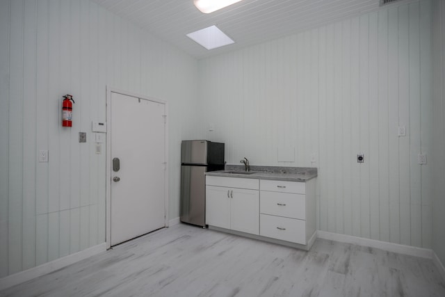 interior space with sink, a skylight, light wood-type flooring, stainless steel refrigerator, and white cabinets