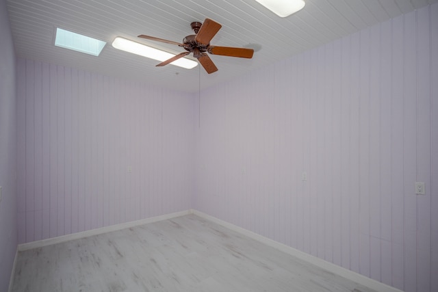 unfurnished room with ceiling fan, a skylight, and wood-type flooring