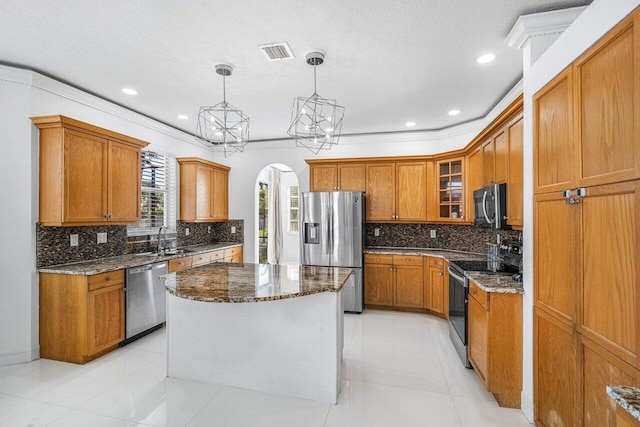 kitchen featuring pendant lighting, a center island, stainless steel appliances, dark stone countertops, and crown molding