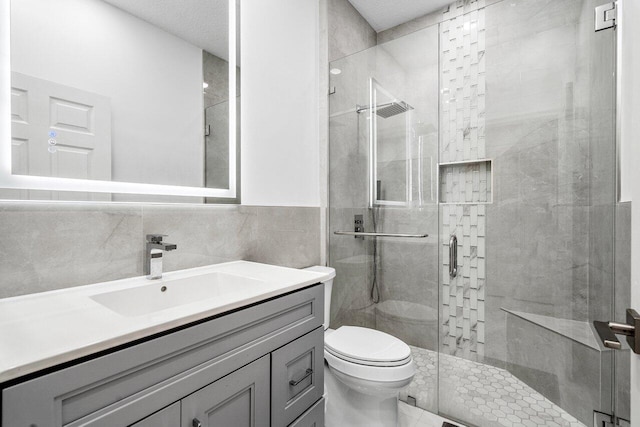 bathroom featuring a shower with shower door, vanity, tile walls, and toilet