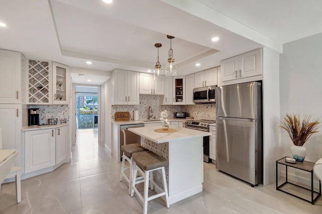 kitchen with white cabinets, a kitchen island, stainless steel appliances, hanging light fixtures, and a tray ceiling