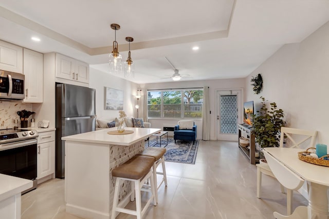 kitchen with tasteful backsplash, pendant lighting, appliances with stainless steel finishes, a breakfast bar area, and white cabinets