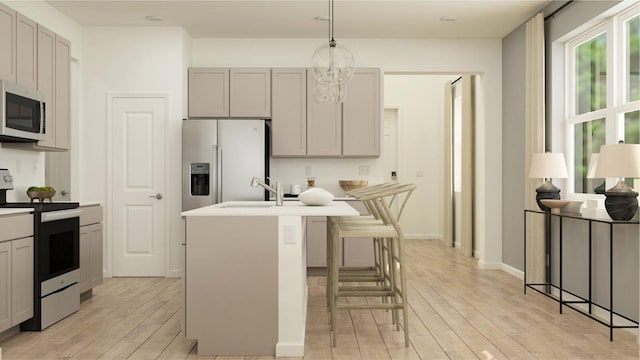 kitchen featuring a breakfast bar, appliances with stainless steel finishes, gray cabinets, and an island with sink