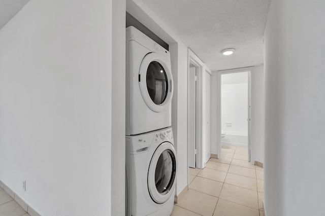 laundry room featuring stacked washer / drying machine, light tile patterned flooring, and a textured ceiling